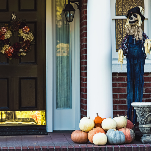 Front porch with a scarecrow, pumpkins, and a fall wreath, perfect for transitioning fall decor from Halloween to Thanksgiving.