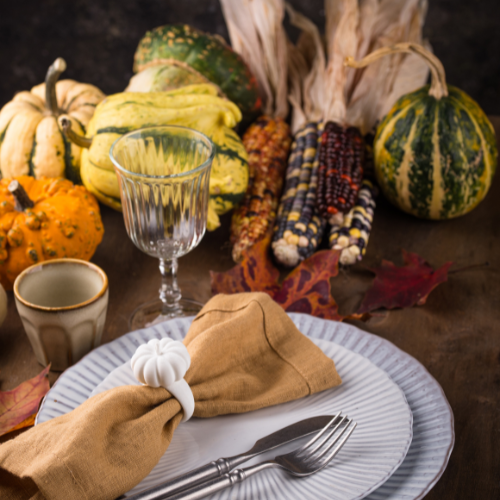 Fall kitchen table with pumpkins, gourds, and autumn-inspired decor, including a linen napkin and glassware.