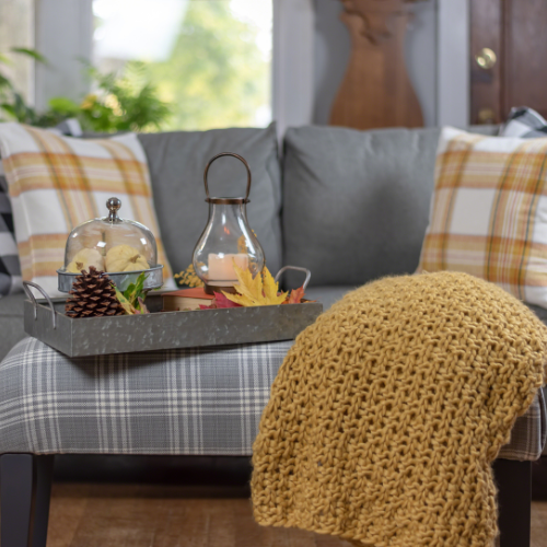 Living room with fall throw pillows, a chunky knit blanket, and a metal tray with a lantern centerpiece for autumn.