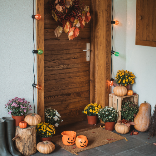 Front porch decorated with pumpkins, potted flowers, and string lights for a festive fall and Halloween look.