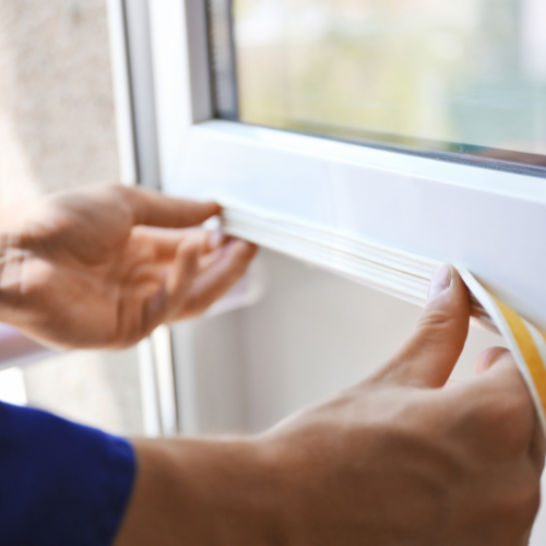 Applying weatherstripping to seal a drafty window before winter.