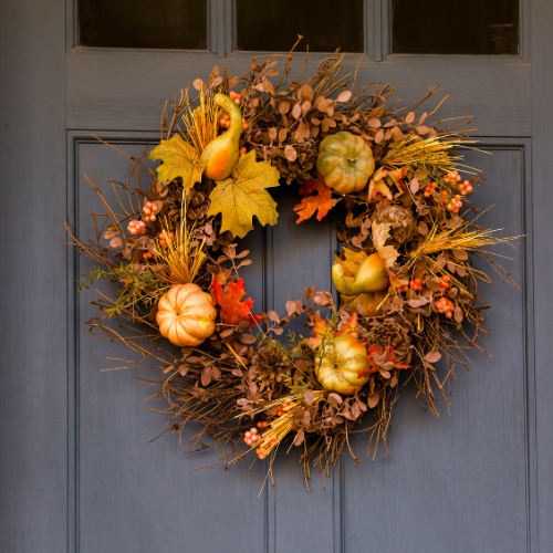 Fall wreath with pumpkins, leaves, and berries hanging on a door, perfect for autumn decor.