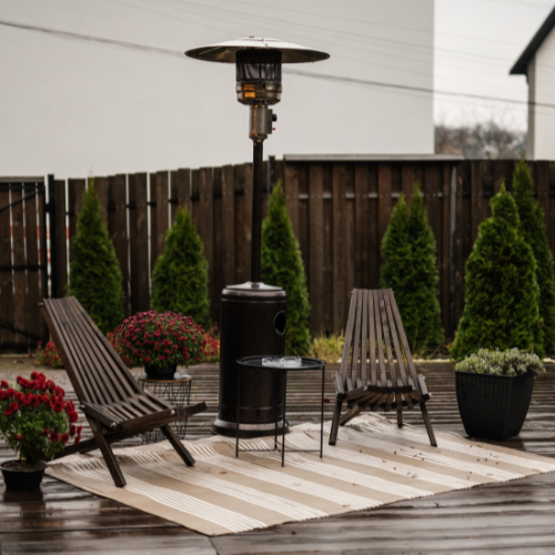 Freestanding propane heater on a patio with wooden chairs.